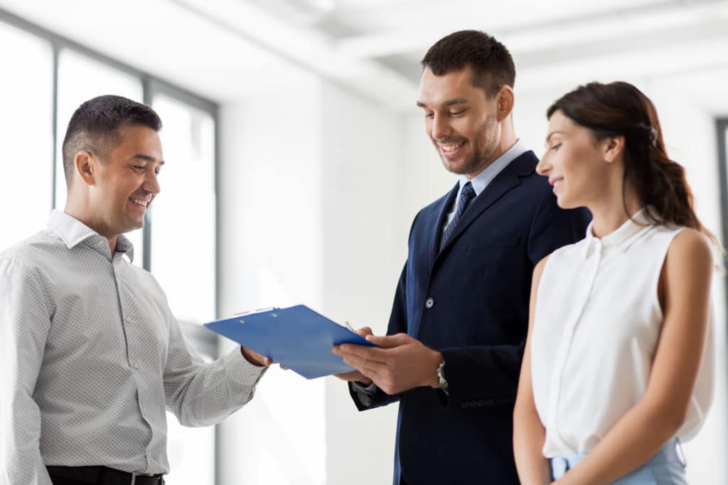 Real Estate Business Sale And People Concept Male Realtor With Clipboard And Pen Showing Contract Document To Customers At New Office Room Realtor